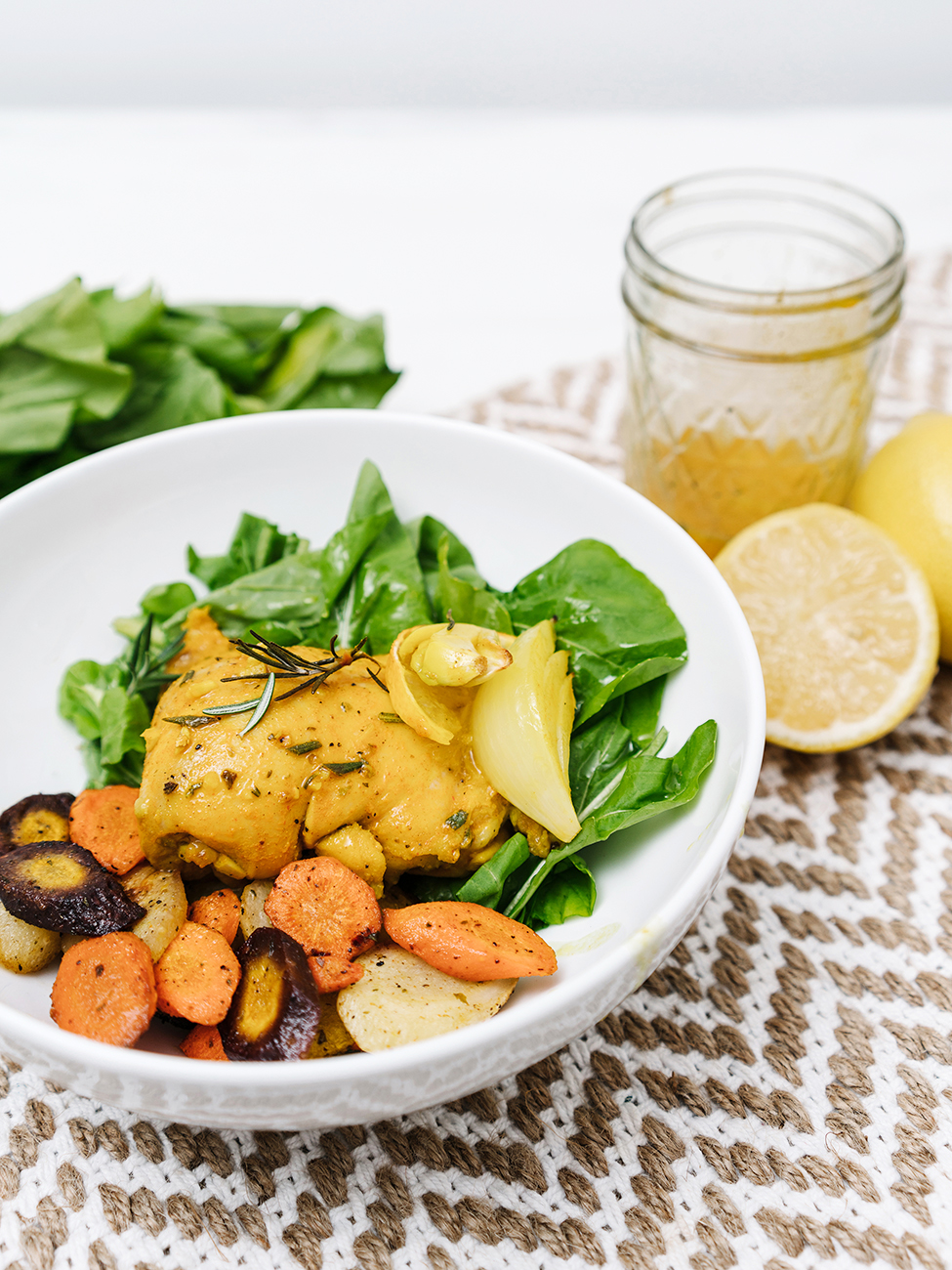 Lemon garlic chicken thigh on a white plate with roasted vegetables and greens